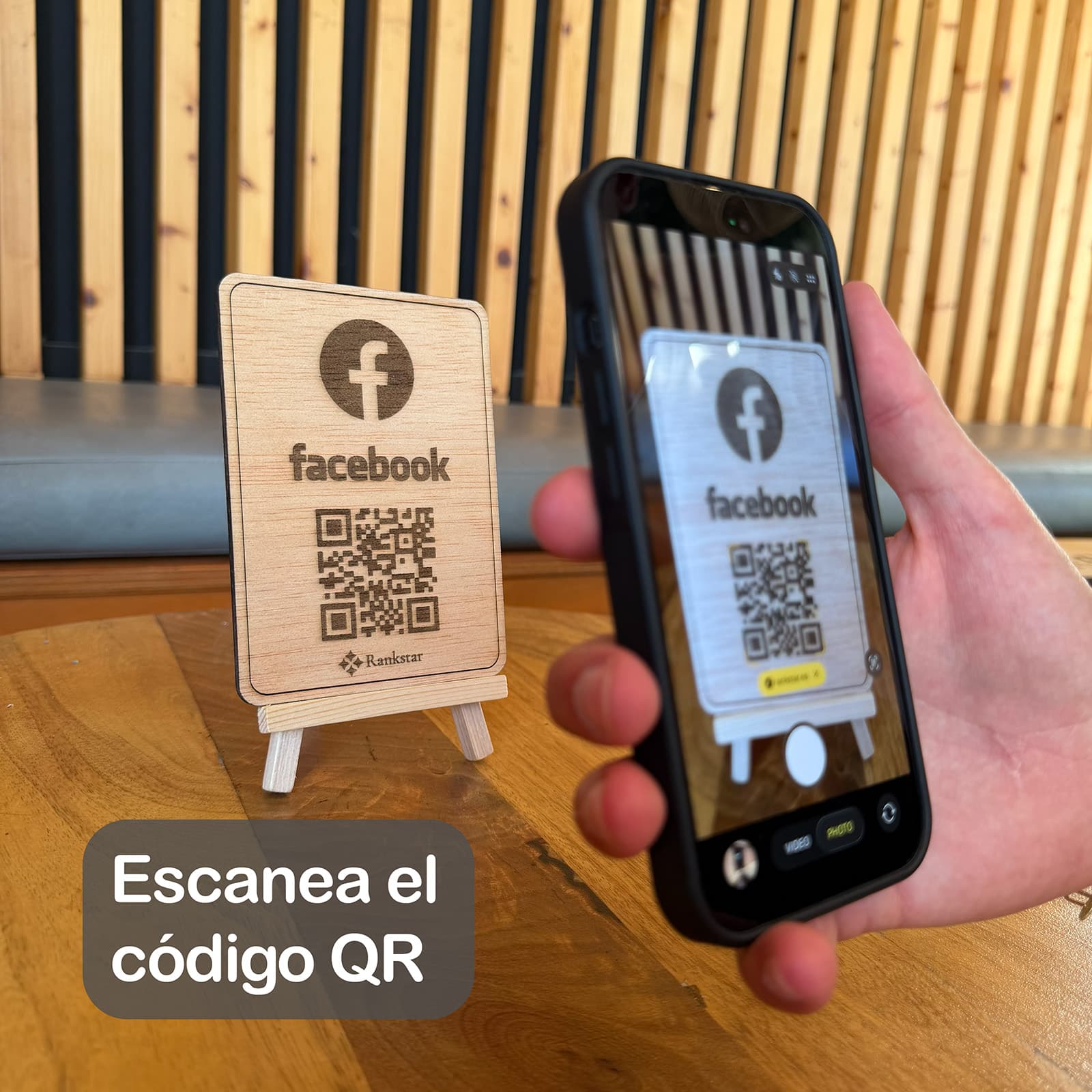 Una mano escanea con el móvil el QR del expositor Rankstar de Facebook sobre la mesa de un local, con el rótulo «Escanea el código QR»