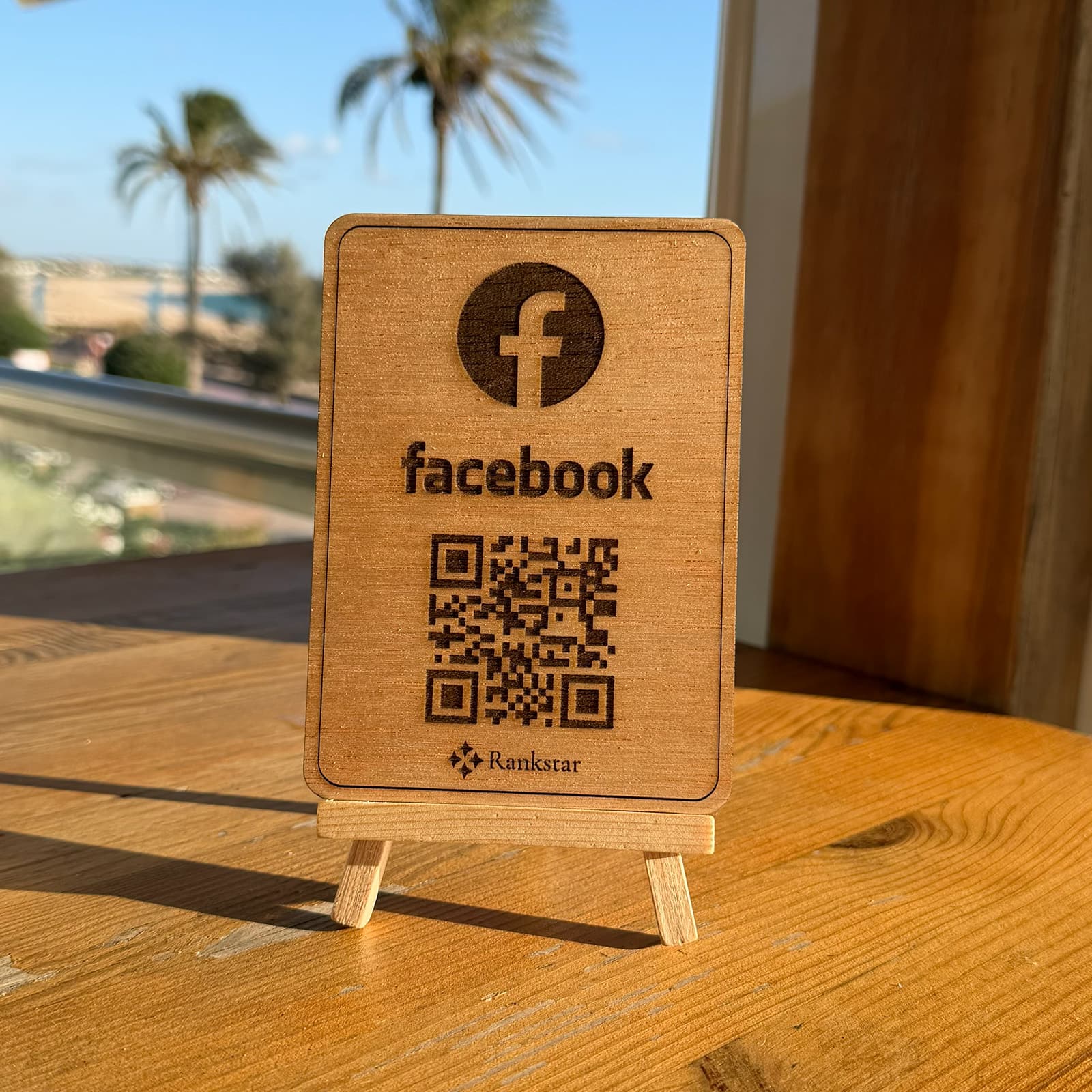 Expositor Rankstar de Facebook sobre la mesa de una terraza, con palmeras y el mar al fondo