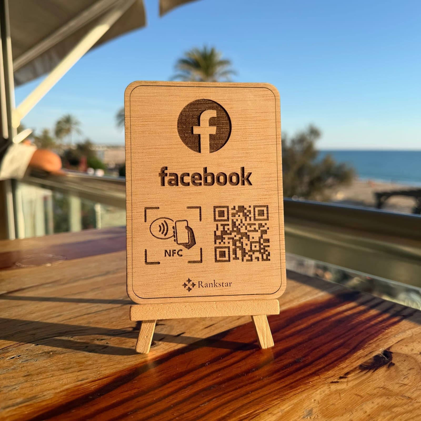 Expositor Rankstar de Facebook en la mesa de una terraza, con palmeras y el mar al fondo