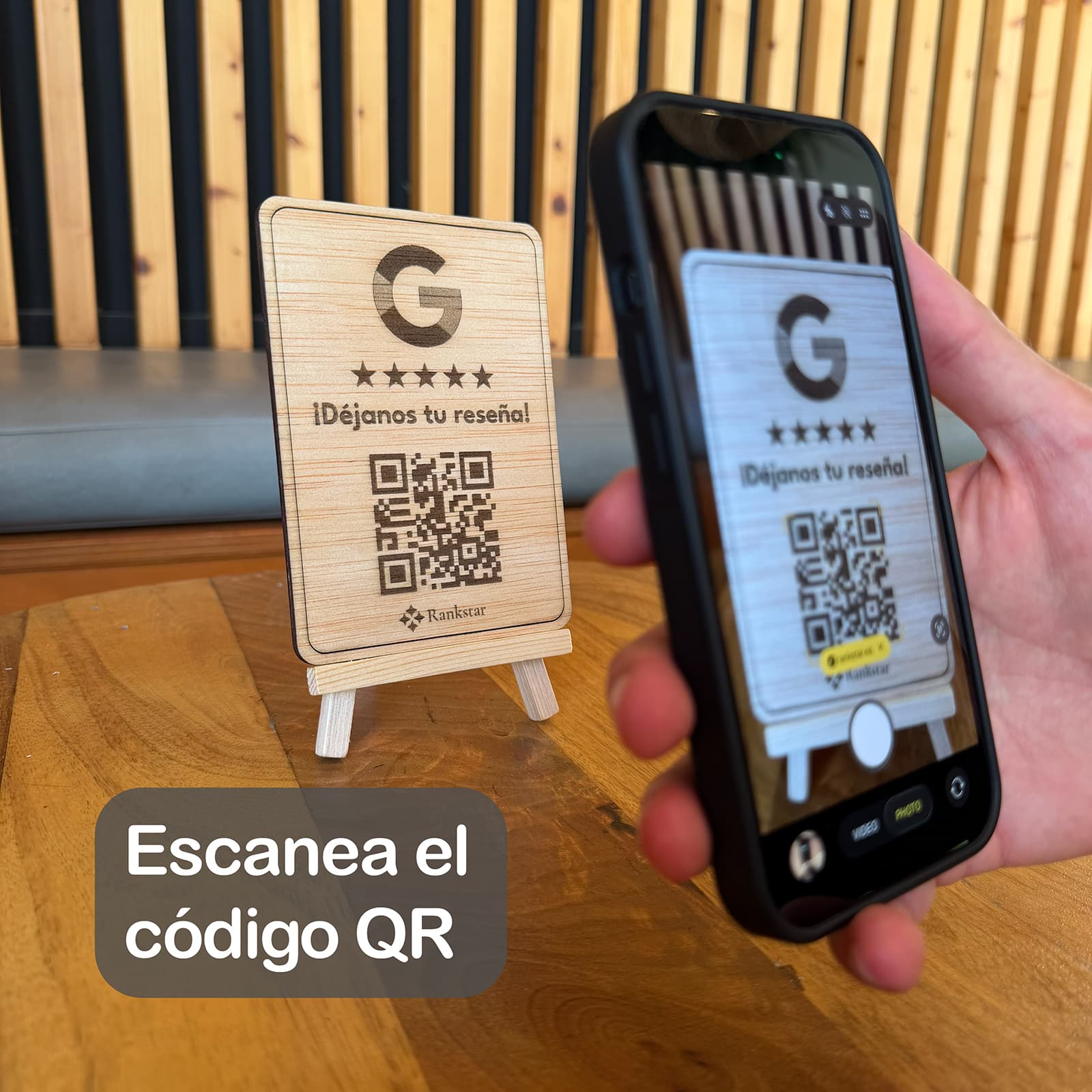 Una mano escanea con el móvil el QR del expositor Rankstar de Google sobre la mesa de un local, con el rótulo «Escanea el código QR»