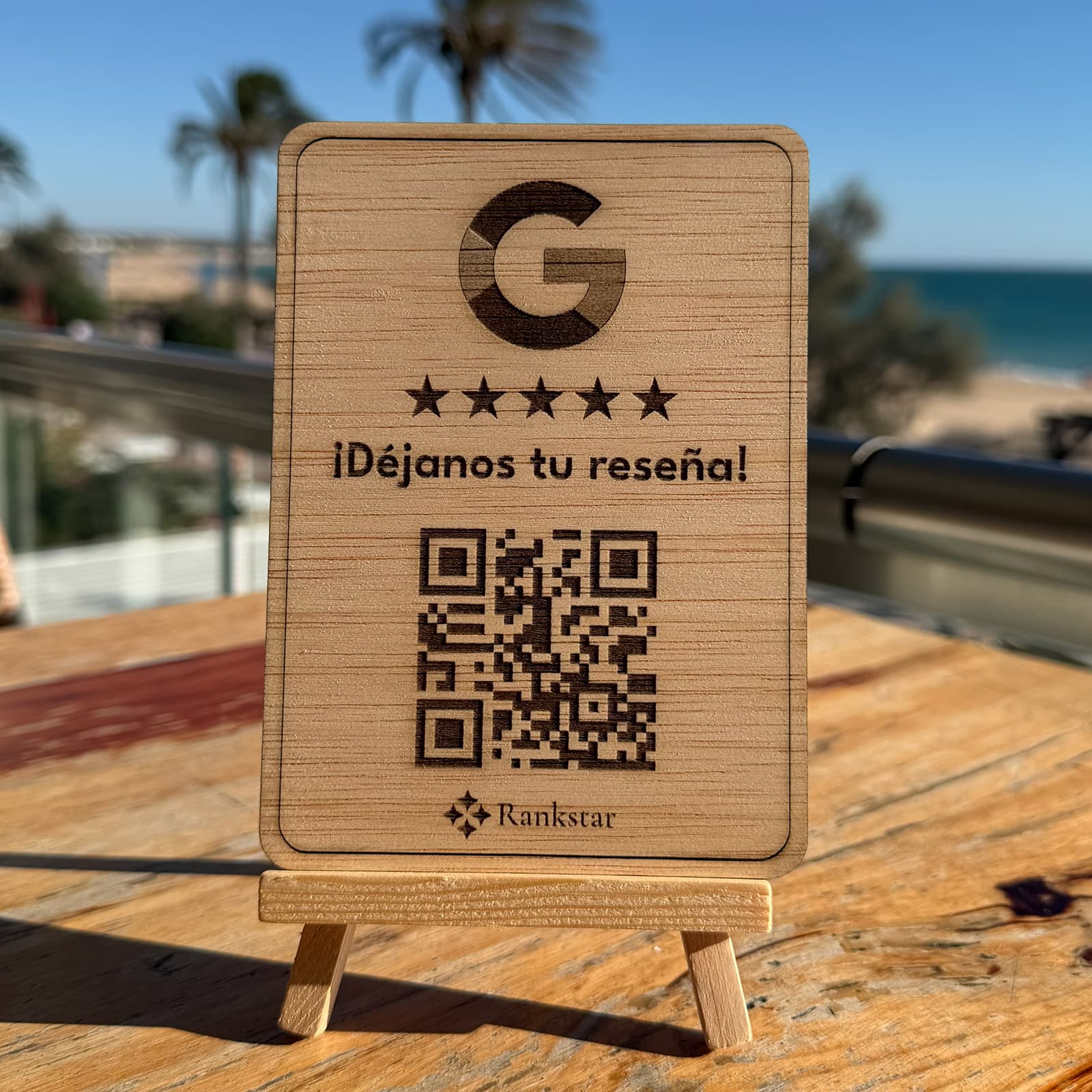 Expositor Rankstar de Google sobre la mesa de una terraza, con palmeras y el mar al fondo