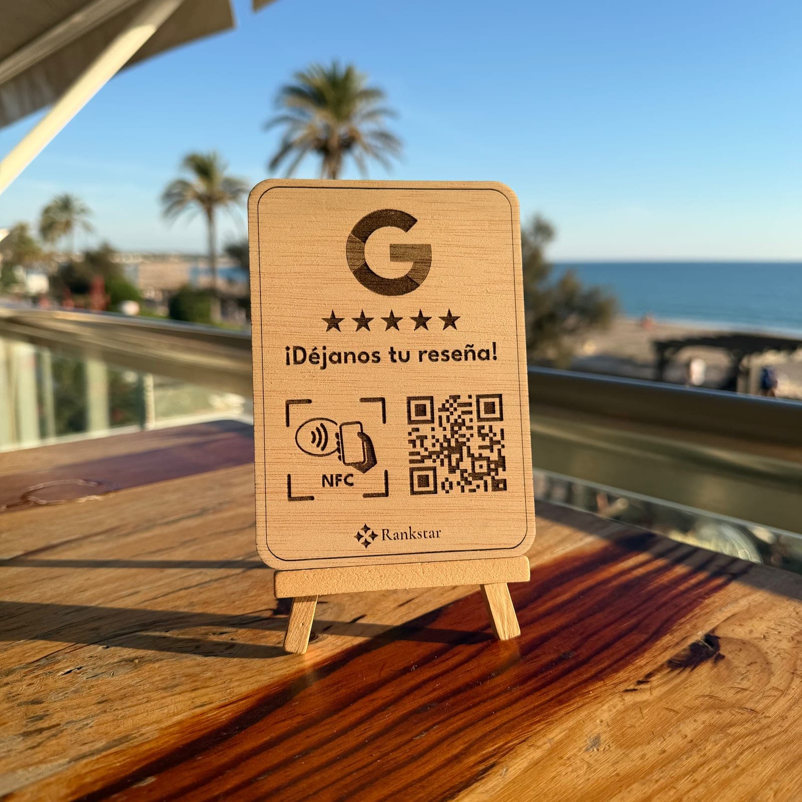 Expositor Rankstar de Google sobre la mesa de una terraza, con palmeras y el mar al fondo
