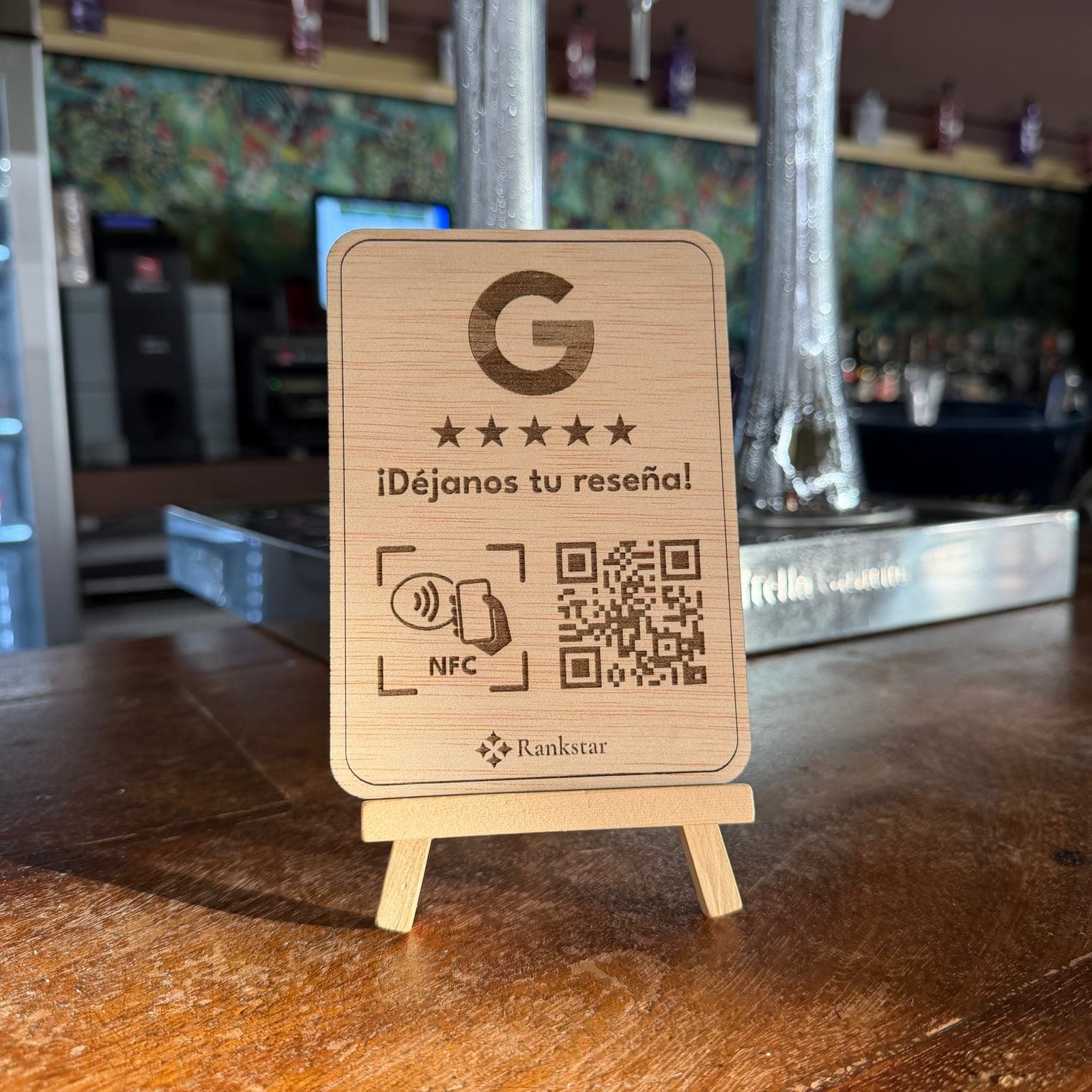 Expositor Rankstar de reseñas de Google en la barra de un bar, con el grifo de cerveza y la pared de papel pintado verde detrás