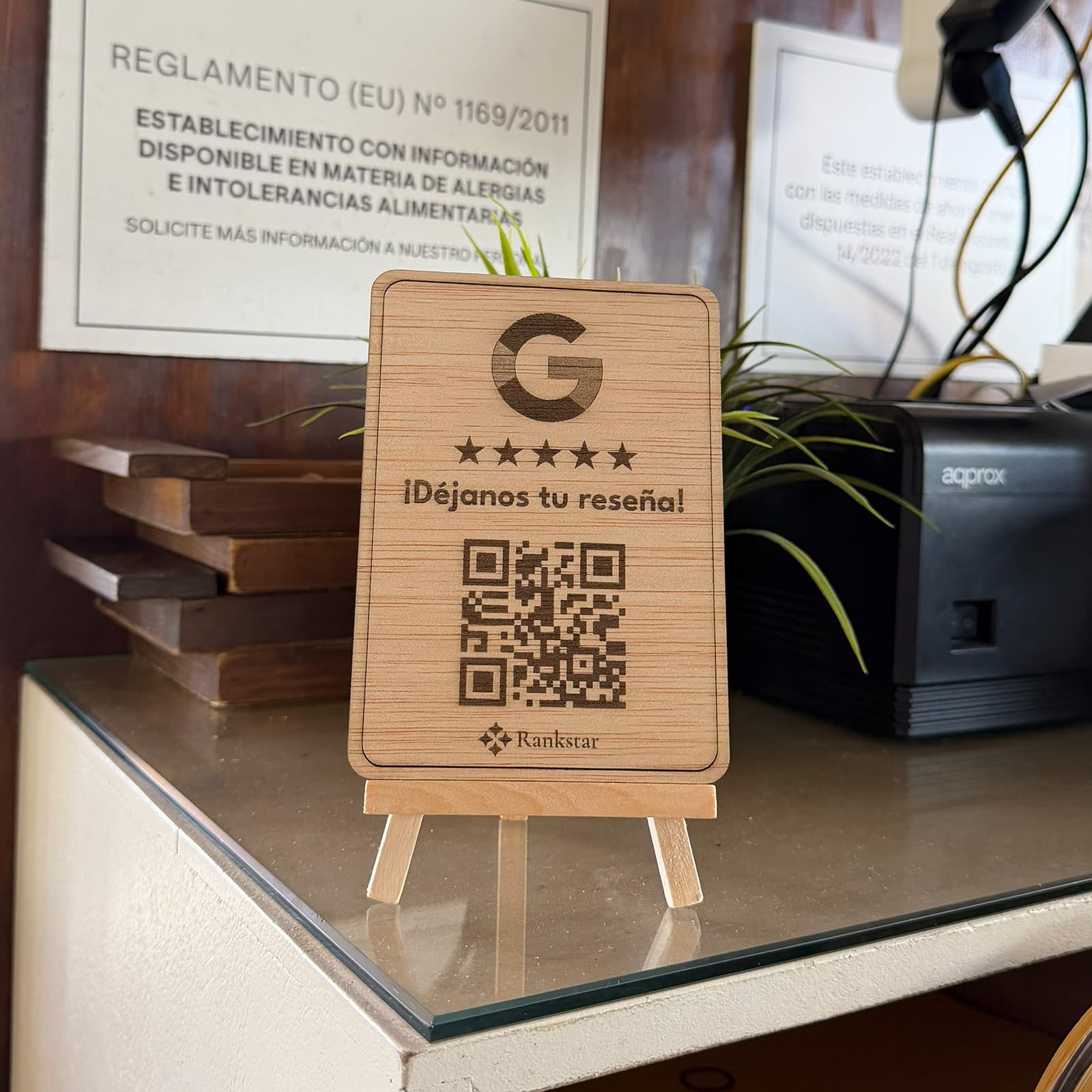Expositor Rankstar de Google sobre un mostrador de cristal, junto al cartel de alérgenos y la impresora de tiques