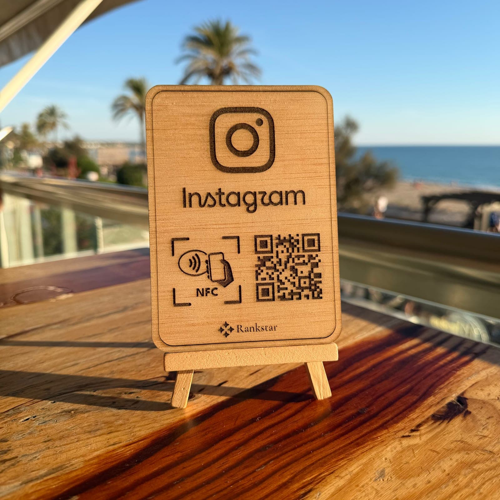 Expositor Rankstar de Instagram sobre la mesa de una terraza, con palmeras y el mar al fondo