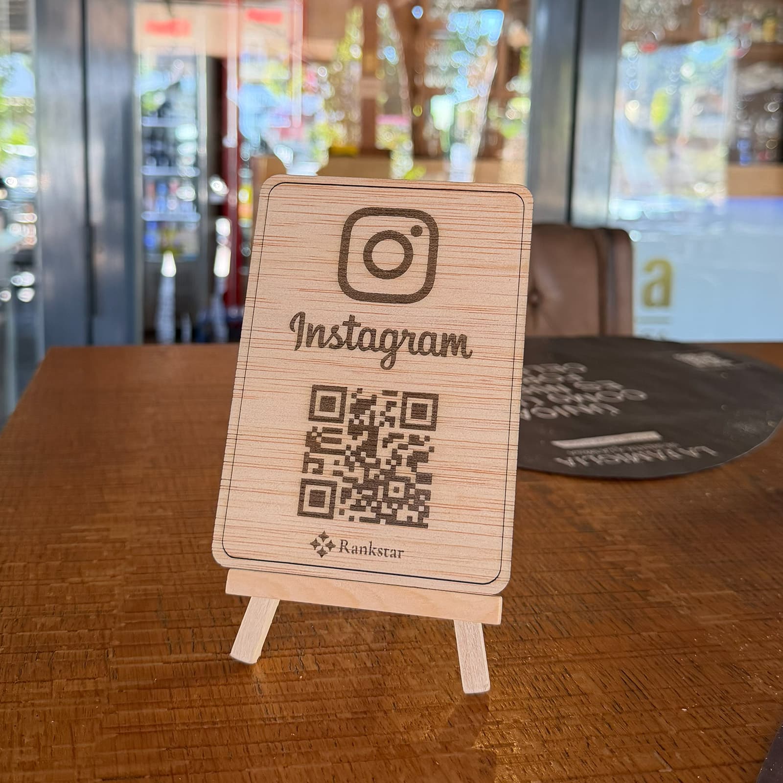 Expositor Rankstar de Instagram sobre una mesa de madera en el salón de un restaurante, con los ventanales al fondo
