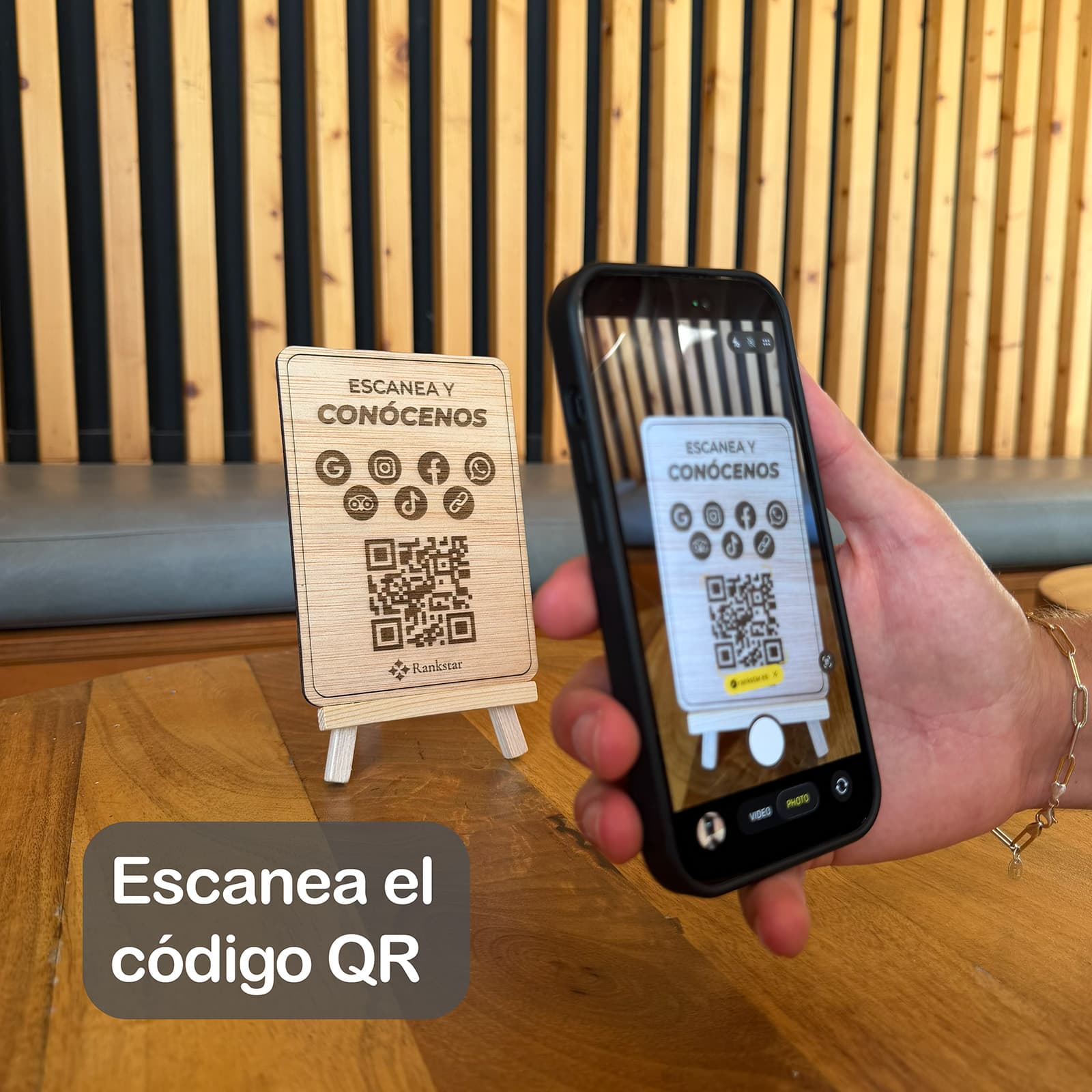 Una mano escanea con el móvil el QR del expositor Rankstar Multilink sobre la mesa de un local, con el rótulo «Escanea el código QR»