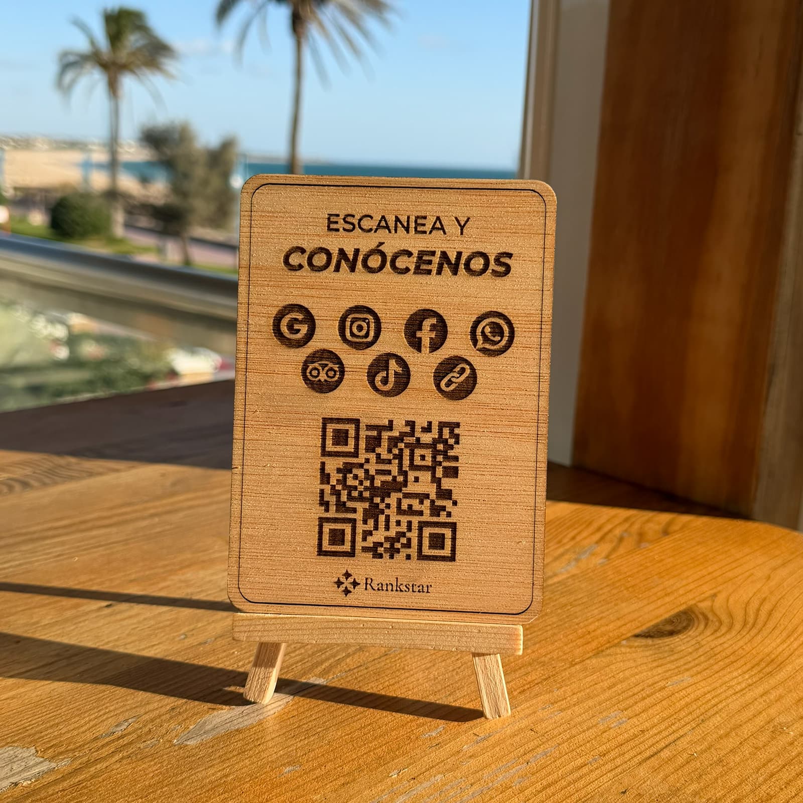 Expositor Rankstar Multilink sobre la mesa de una terraza, con palmeras y el mar al fondo