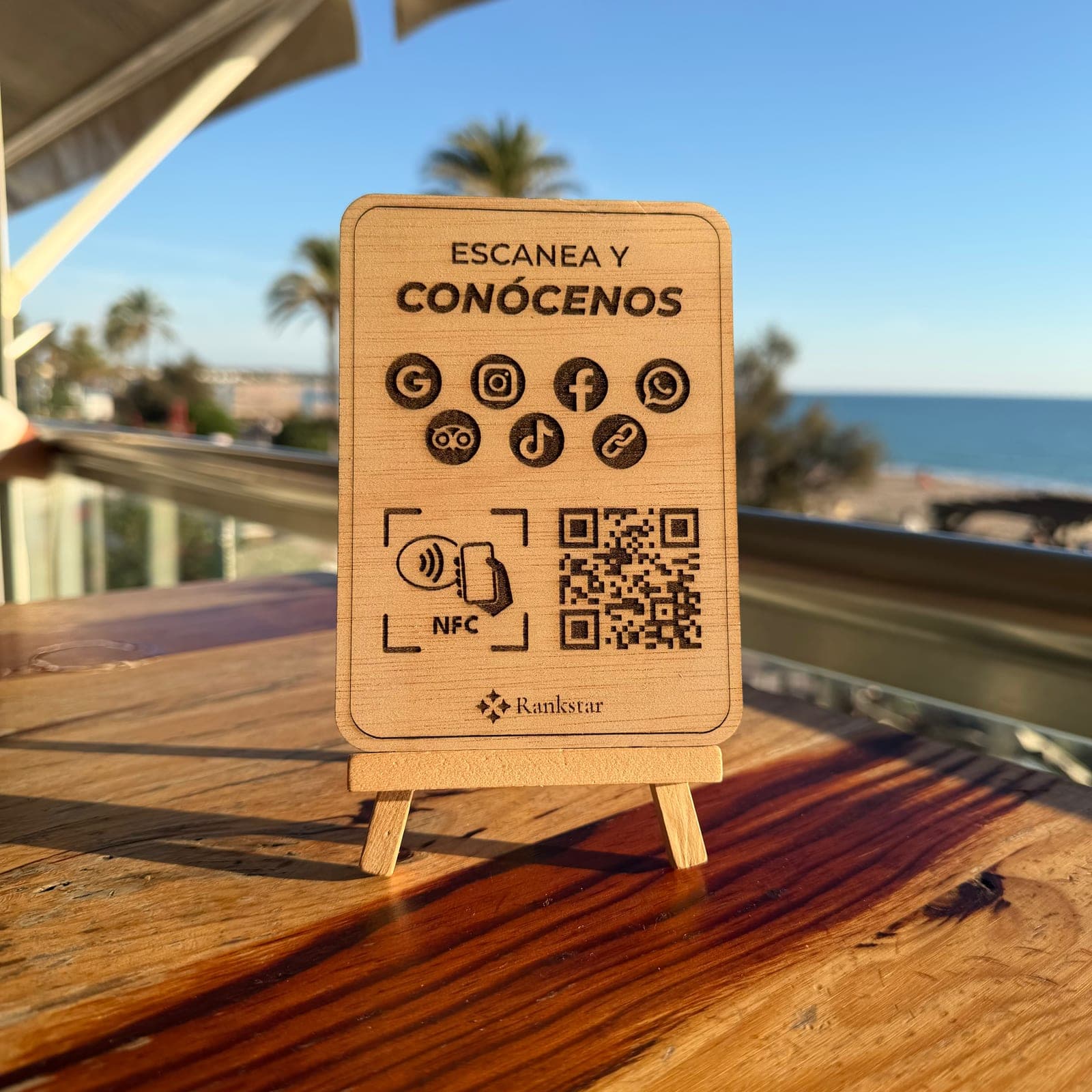 Expositor Rankstar Multilink en la mesa de una terraza, con palmeras y el mar al fondo