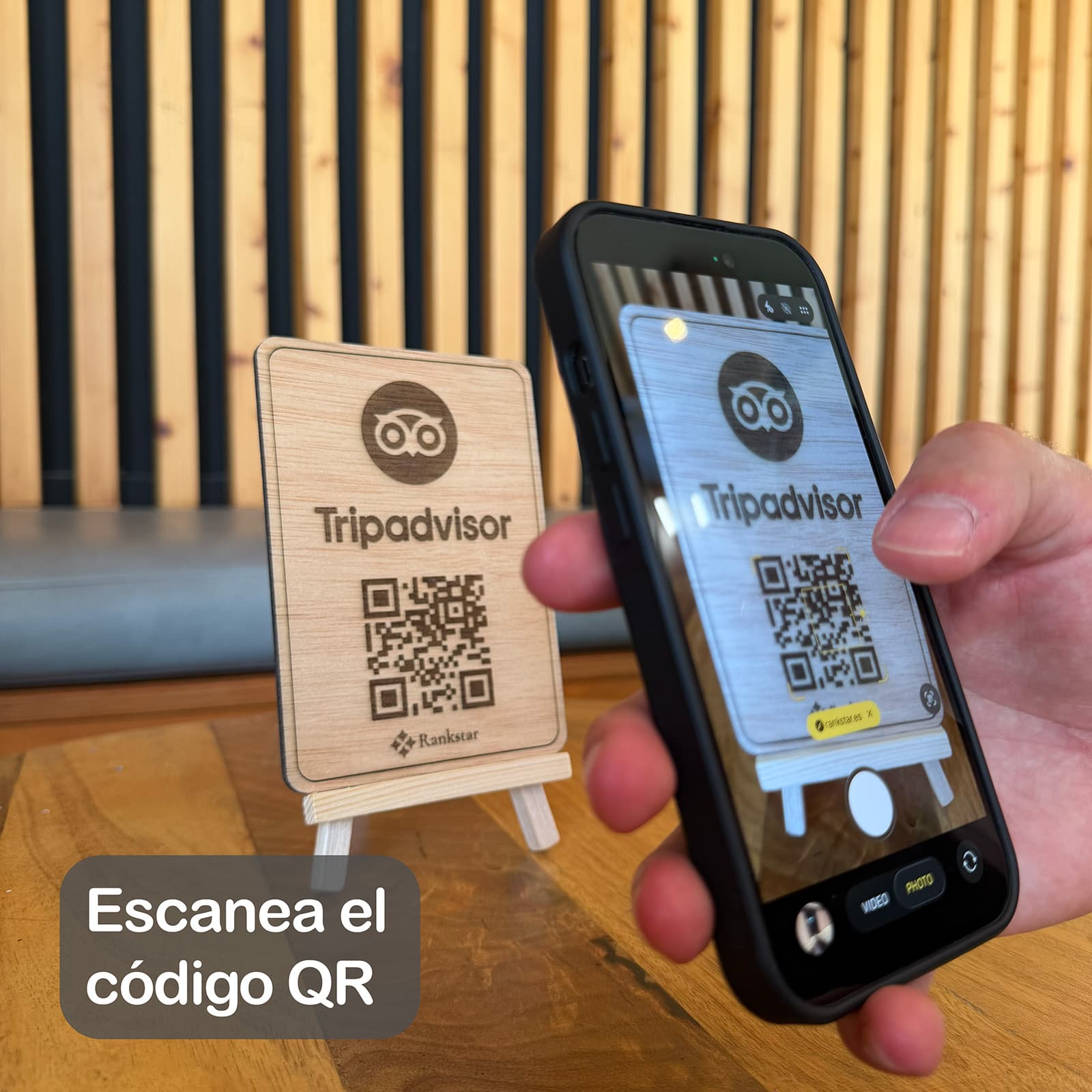 Una mano escanea con el móvil el QR del expositor Rankstar de Tripadvisor sobre la mesa de un local, con el rótulo «Escanea el código QR»
