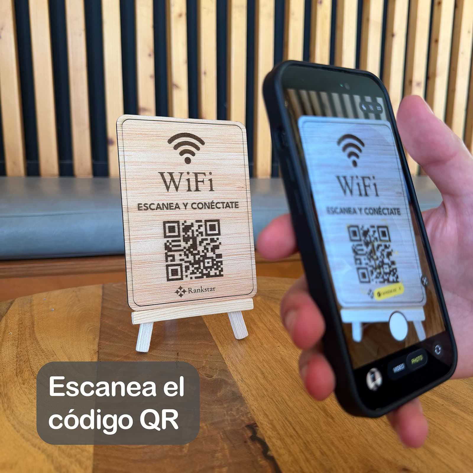 Una mano escanea con el móvil el QR del expositor Rankstar de WiFi sobre la mesa de un local, con el rótulo «Escanea el código QR»
