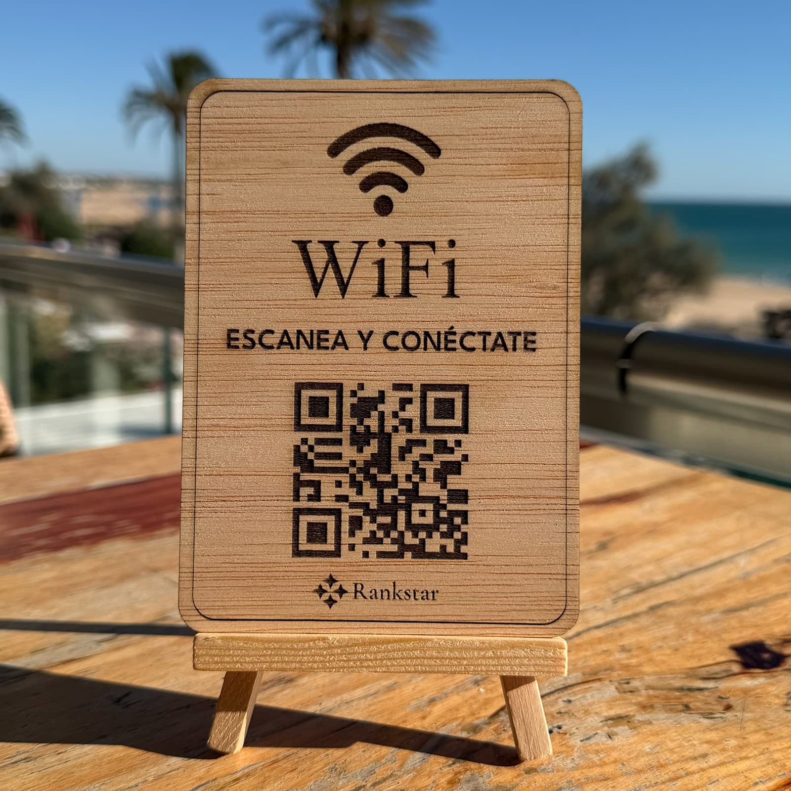 Expositor Rankstar de WiFi sobre la mesa de una terraza, con palmeras y el mar al fondo
