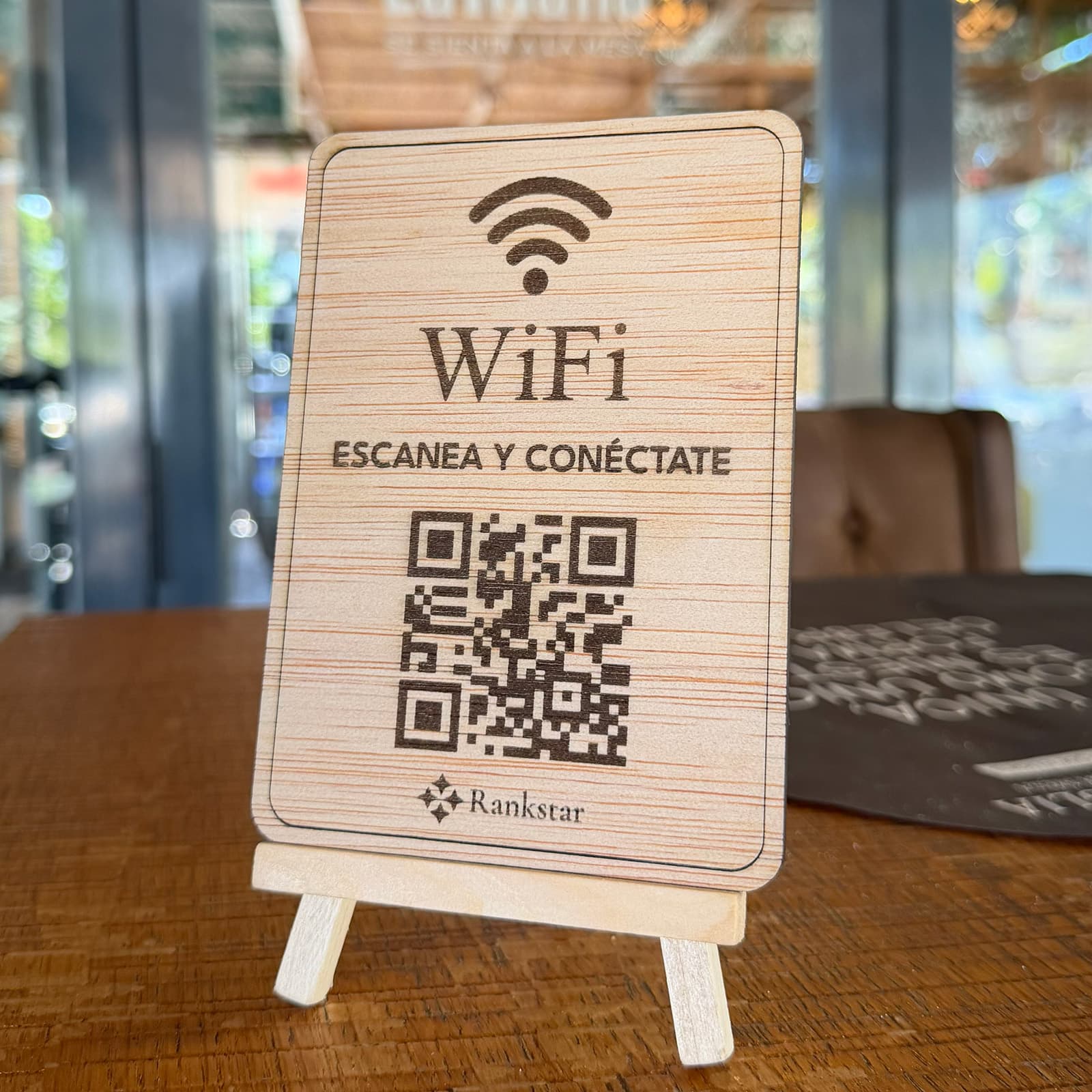 Expositor Rankstar de WiFi sobre una mesa de madera en el salón de un restaurante, con los ventanales al fondo