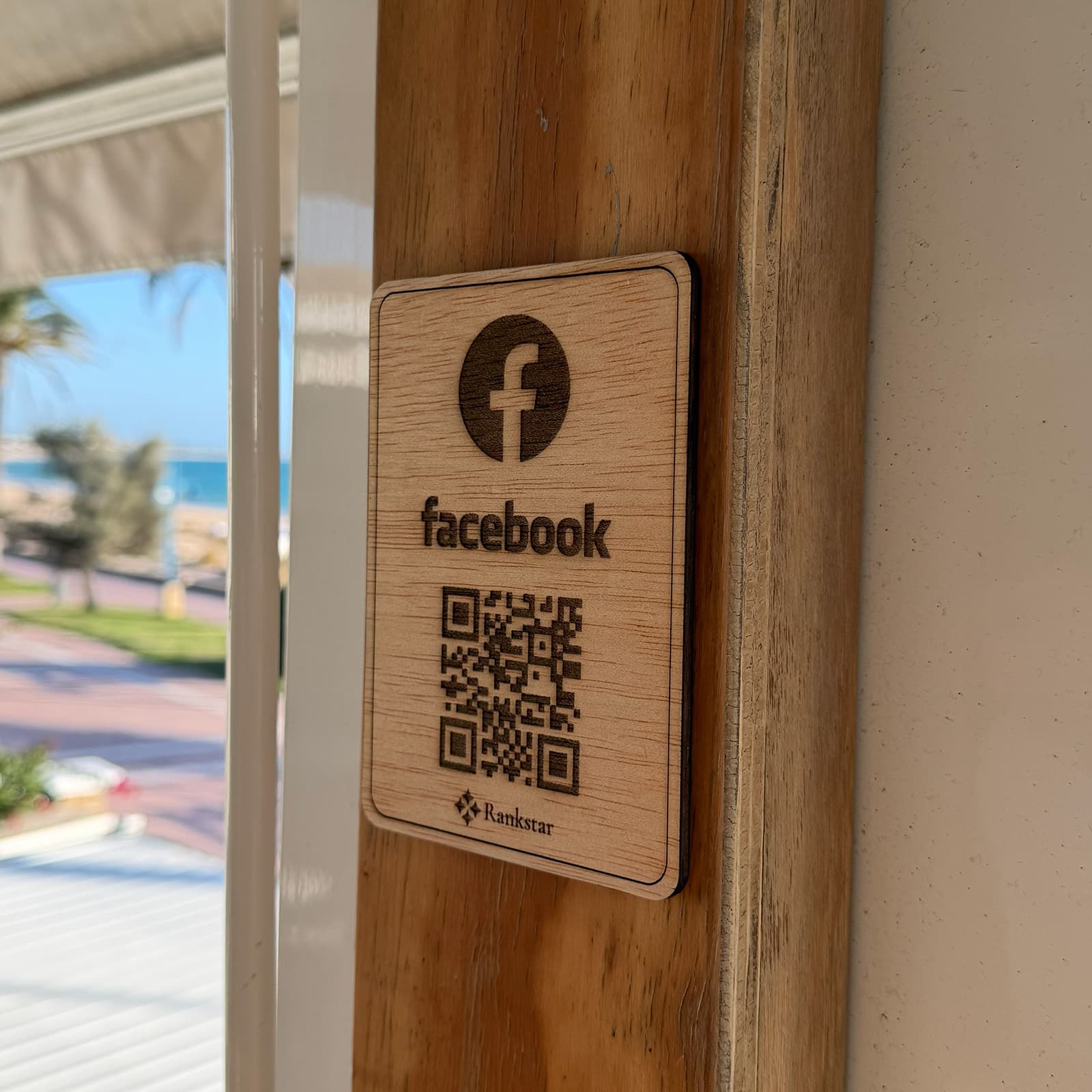 Placa Rankstar de Facebook pegada en el poste de madera de un chiringuito, con el paseo marítimo al fondo