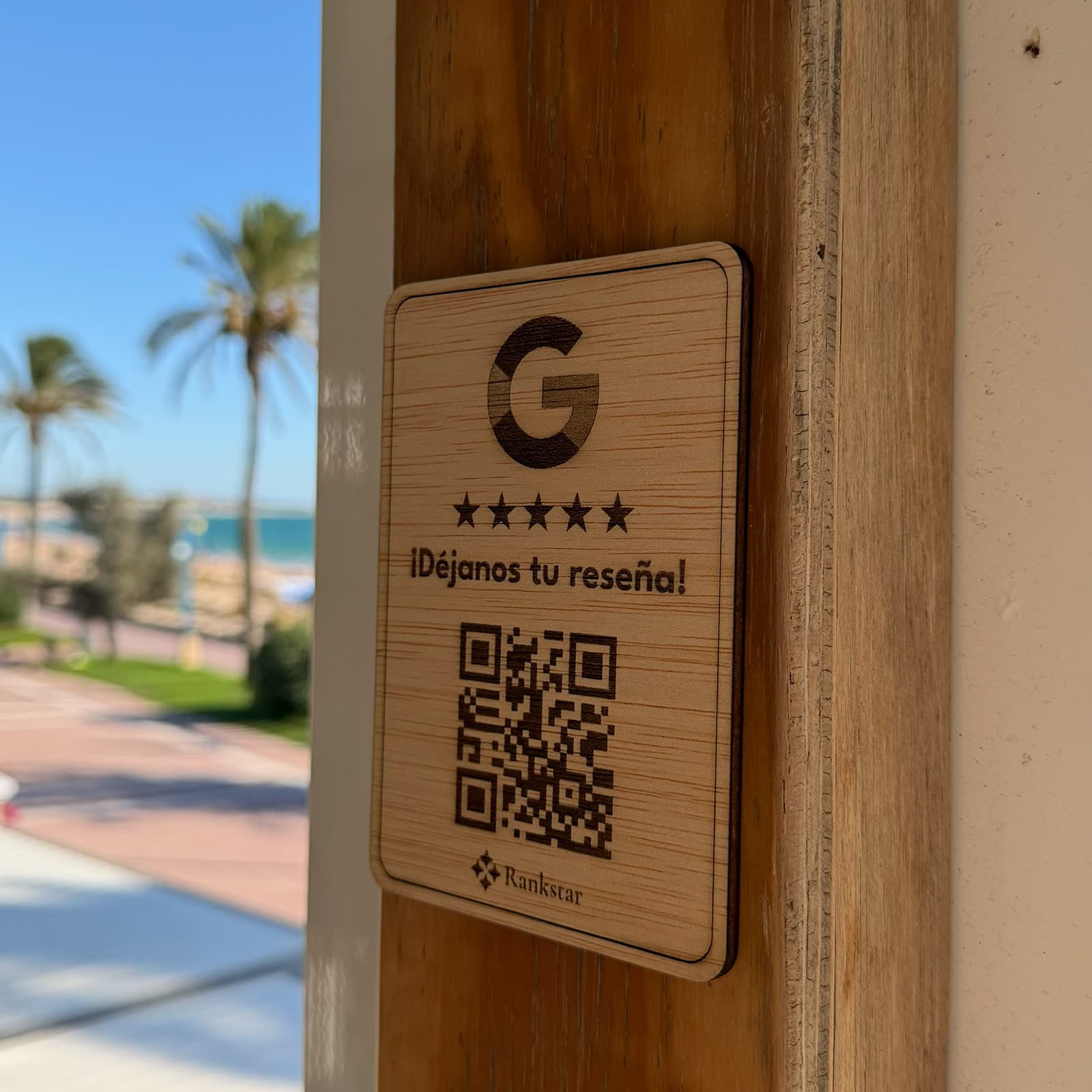 Placa Rankstar de reseñas de Google pegada en el poste de madera de un chiringuito, con el paseo marítimo al fondo