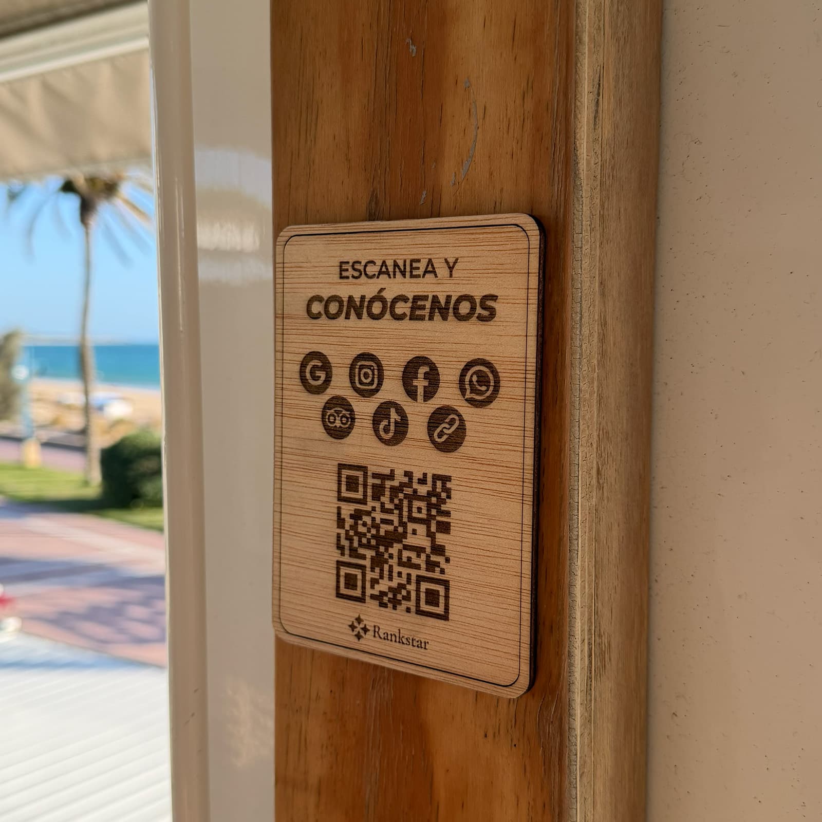 Placa Rankstar Multilink pegada en el poste de madera de un chiringuito, con el paseo marítimo al fondo