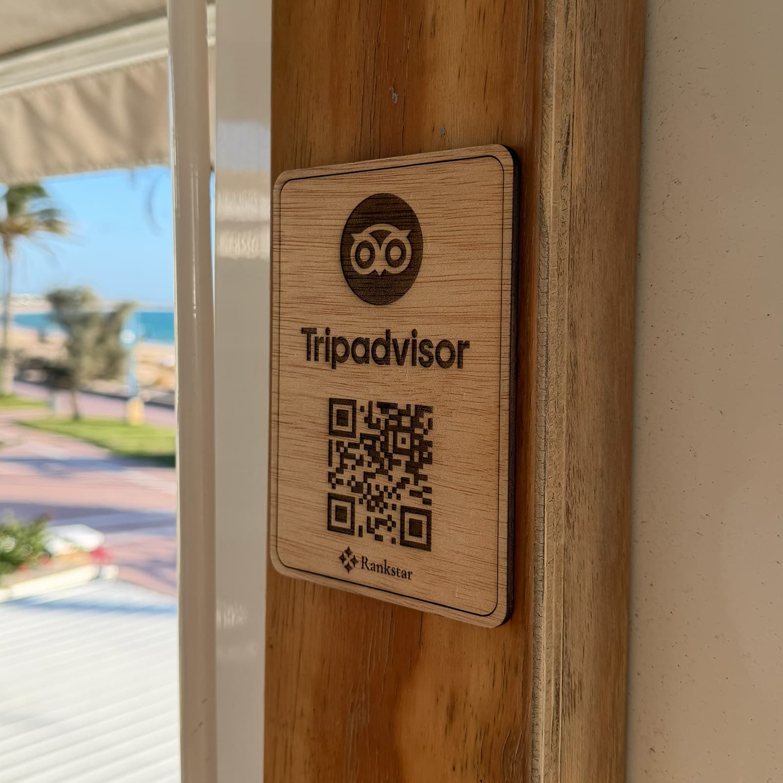 Placa Rankstar de Tripadvisor pegada en el poste de madera de un chiringuito, con el paseo marítimo al fondo