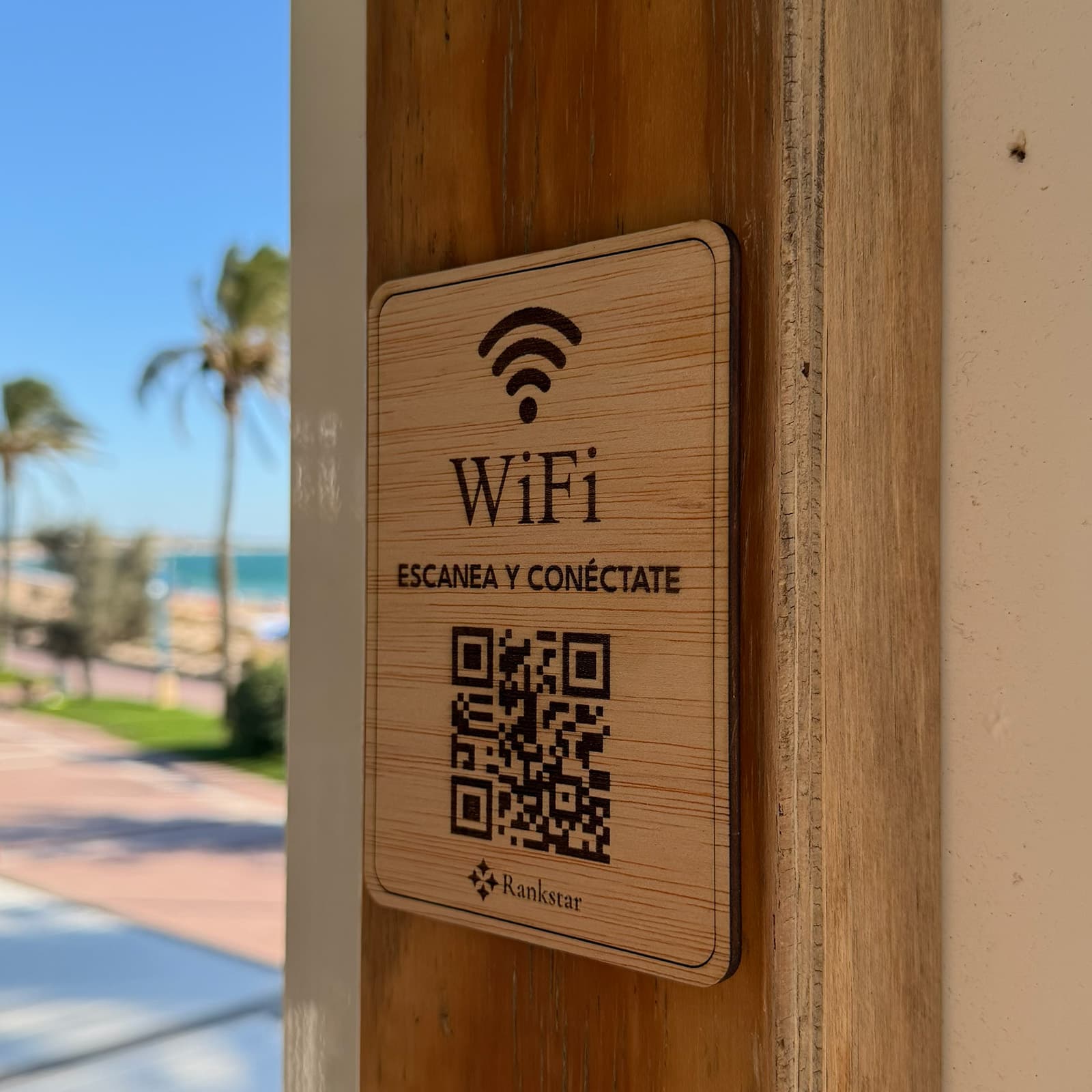 Placa Rankstar de WiFi pegada en el poste de madera de un chiringuito, con el paseo marítimo al fondo