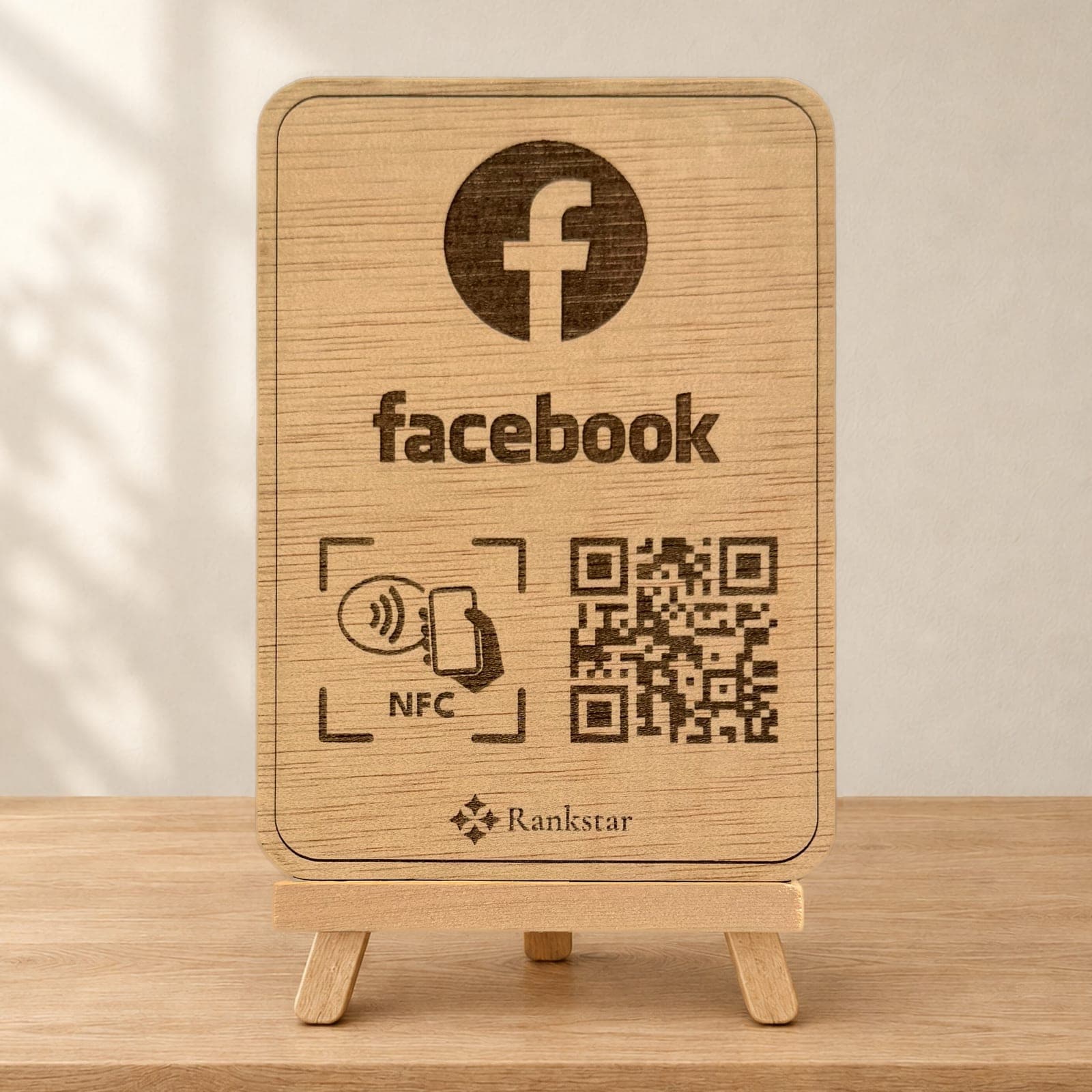 Expositor Rankstar de madera sobre su caballete, con el logo de Facebook, el símbolo NFC y el QR grabados a láser, sobre una mesa de madera clara junto a una pared con sombras de hojas